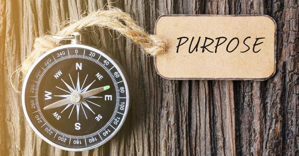 Magnetic compass and paper tag written with PURPOSE text on old wooden background. A concept. www.clemmergroup.com